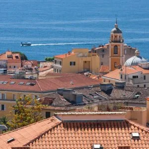 Vue sur les toits rouges d’Ajaccio avec la mer Méditerranée en arrière-plan et une église baroque au centre de l’image.